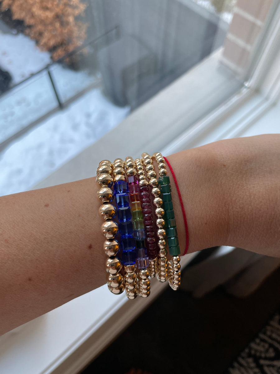 mixed stack. Left to right- 8mm 14k gold filled bracelet, 6mm with cobalt blue larger Swarovski crystal cubes, 5mm with rainbow Swarovski crystal cubes, 4mm with natural faceted rubies and clasp, 5mm 14k gold filled bracelet, 4mm 14k gold filled bracelet with opaque green Swarovski crystal beads.  